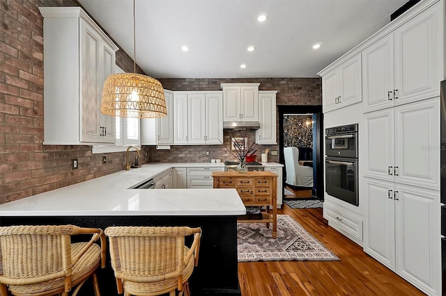 kitchen with wood finished floors, brick wall, a peninsula, white cabinets, and dobule oven black