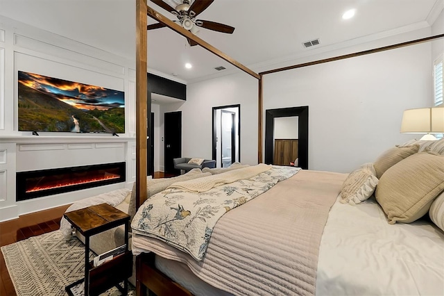 bedroom with a glass covered fireplace, wood finished floors, visible vents, and ornamental molding