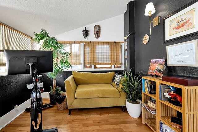 interior space with lofted ceiling, a textured ceiling, a healthy amount of sunlight, and wood finished floors