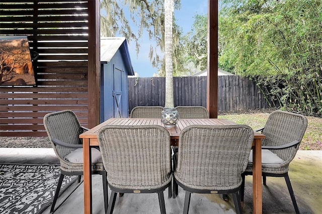 view of patio / terrace with an outbuilding, a shed, outdoor dining space, and a fenced backyard