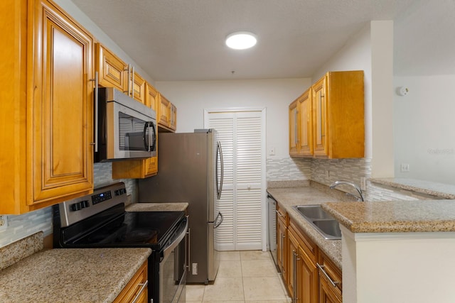 kitchen with appliances with stainless steel finishes, tasteful backsplash, light stone counters, sink, and light tile patterned flooring