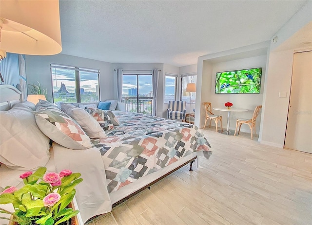 bedroom with access to exterior, light wood-type flooring, and a textured ceiling