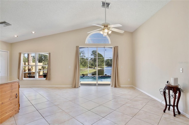 tiled empty room with ceiling fan, lofted ceiling, a textured ceiling, and plenty of natural light