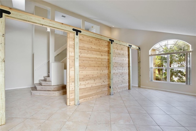 spare room featuring light tile patterned floors, high vaulted ceiling, a barn door, and wood walls