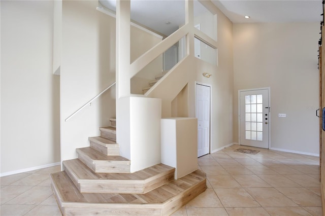 tiled foyer entrance featuring a towering ceiling, a barn door, stairs, and baseboards