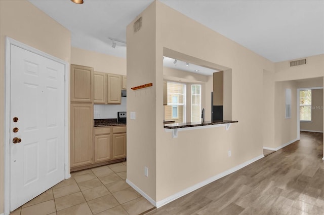 kitchen with kitchen peninsula, light brown cabinetry, rail lighting, backsplash, and dark stone counters