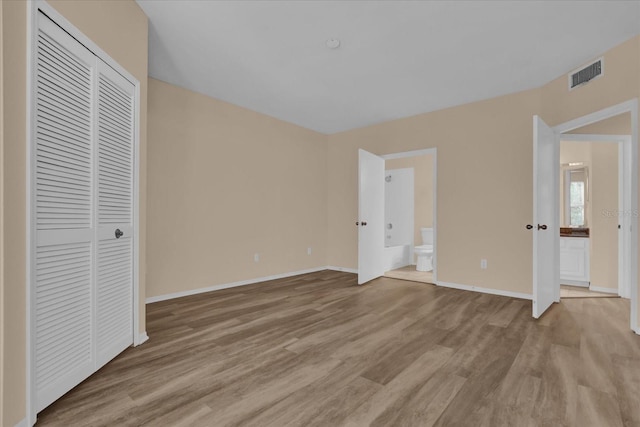 unfurnished bedroom featuring ensuite bath, a closet, and light wood-type flooring