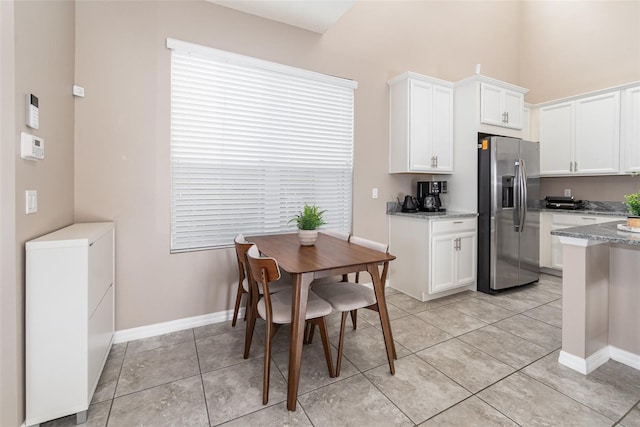 kitchen featuring light stone countertops, stainless steel refrigerator with ice dispenser, light tile patterned floors, and white cabinetry