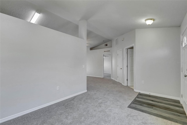 unfurnished room with a textured ceiling, lofted ceiling, and carpet flooring