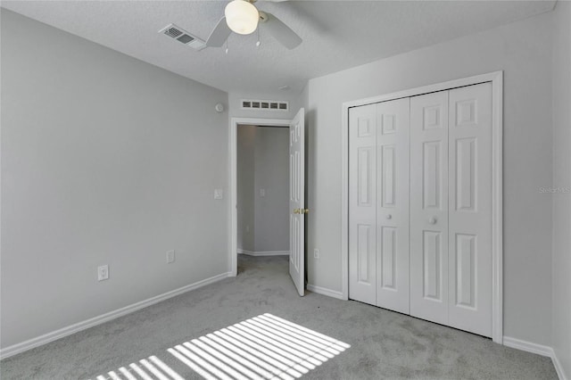 unfurnished bedroom with ceiling fan, light colored carpet, a textured ceiling, and a closet