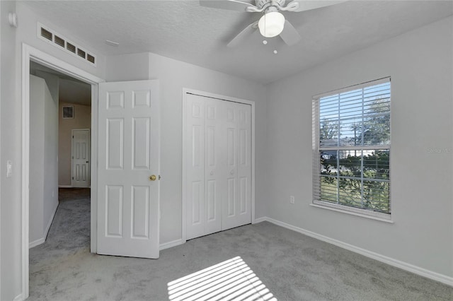 unfurnished bedroom featuring a closet, ceiling fan, a textured ceiling, and light carpet