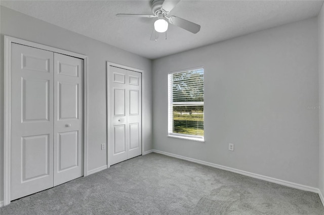 unfurnished bedroom featuring ceiling fan, a textured ceiling, light carpet, and two closets