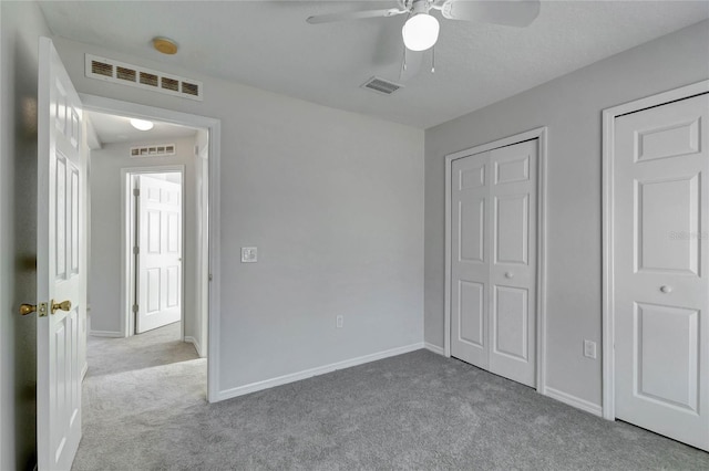 unfurnished bedroom featuring ceiling fan, light carpet, and two closets