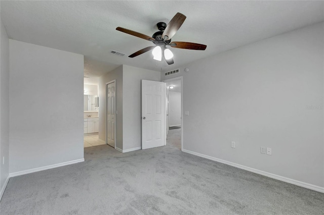 unfurnished bedroom with light carpet, a closet, connected bathroom, and ceiling fan