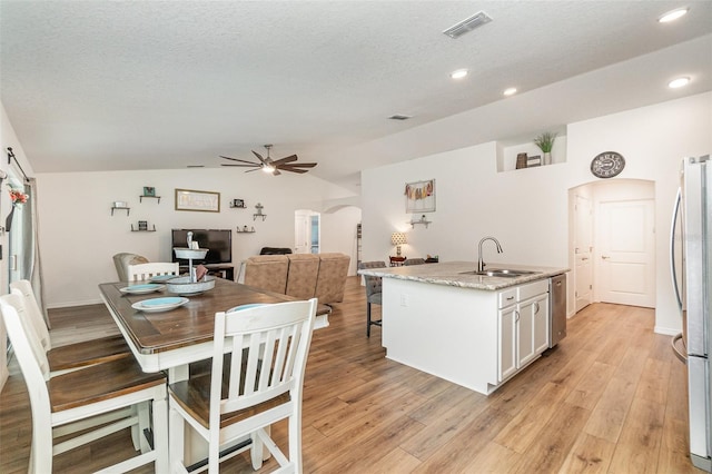 kitchen with stainless steel refrigerator, sink, an island with sink, lofted ceiling, and white cabinets