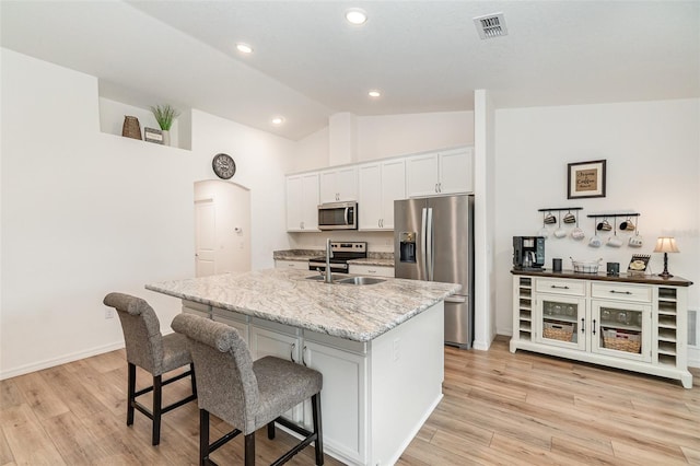 kitchen with white cabinetry, stainless steel appliances, vaulted ceiling, a breakfast bar area, and a kitchen island with sink