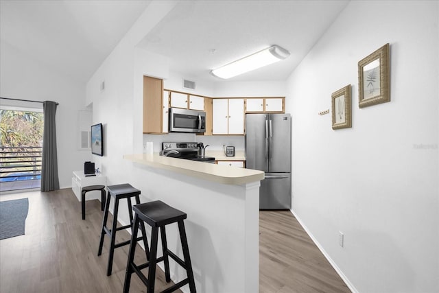 kitchen featuring a breakfast bar area, kitchen peninsula, light hardwood / wood-style floors, and appliances with stainless steel finishes