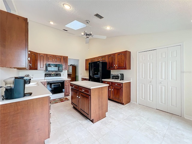 kitchen featuring black appliances, vaulted ceiling with skylight, ceiling fan, a textured ceiling, and a kitchen island