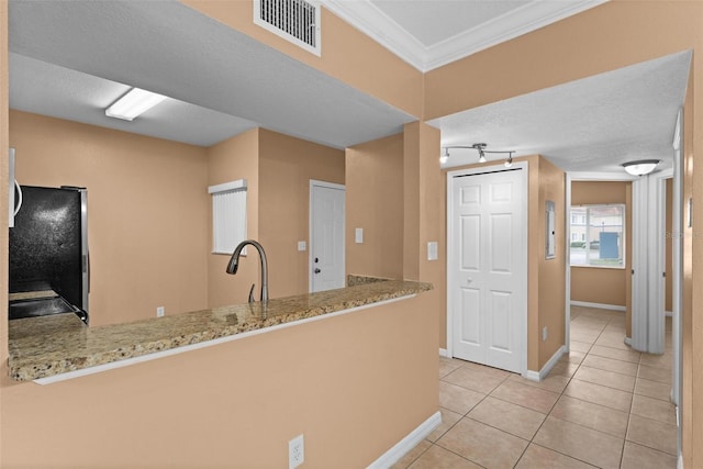 kitchen with light stone countertops, light tile patterned floors, ornamental molding, kitchen peninsula, and stainless steel refrigerator