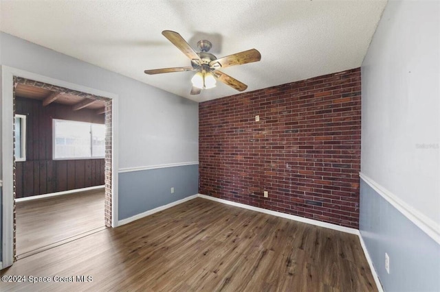 spare room with a textured ceiling, ceiling fan, dark wood-type flooring, and brick wall