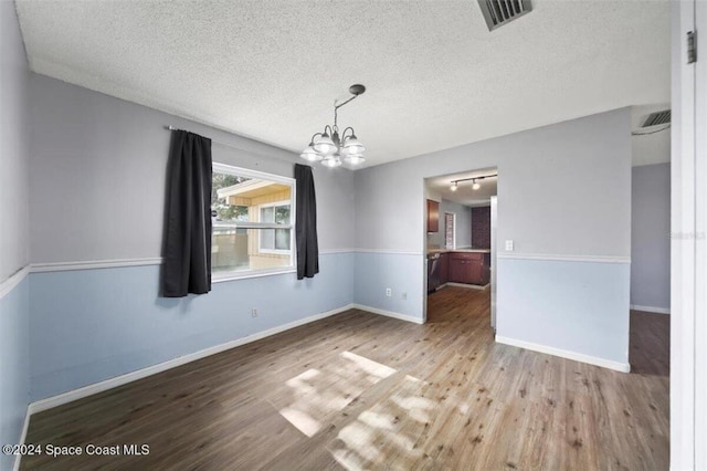 unfurnished dining area with a notable chandelier, light hardwood / wood-style floors, a textured ceiling, and track lighting