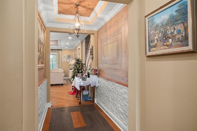 hallway with a raised ceiling, crown molding, wood-type flooring, and an inviting chandelier