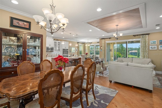 dining area featuring a raised ceiling, light hardwood / wood-style floors, an inviting chandelier, and ornamental molding