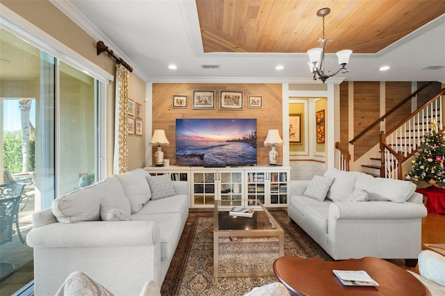 living room with a raised ceiling, wooden walls, ornamental molding, a notable chandelier, and wood ceiling