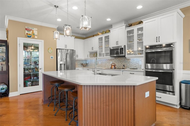 kitchen with white cabinets, hanging light fixtures, an island with sink, appliances with stainless steel finishes, and a breakfast bar area