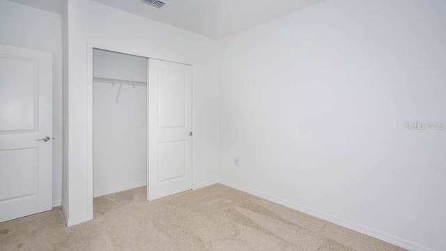 unfurnished bedroom with light carpet and a closet