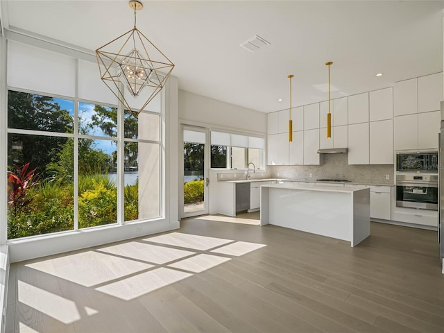 kitchen with backsplash, stainless steel oven, decorative light fixtures, white cabinets, and a center island