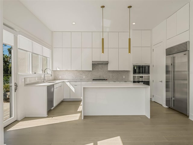 kitchen featuring backsplash, white cabinets, built in appliances, decorative light fixtures, and a kitchen island