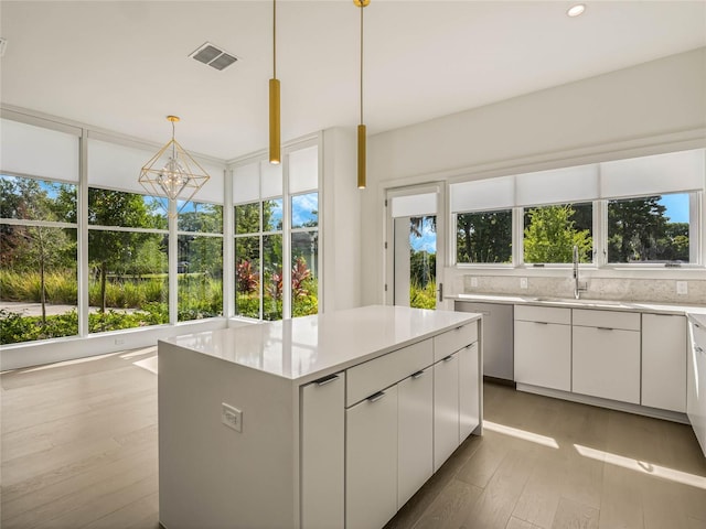 kitchen with pendant lighting, sink, light hardwood / wood-style flooring, a kitchen island, and white cabinetry