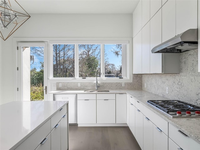 kitchen featuring stainless steel gas stovetop, ventilation hood, sink, hanging light fixtures, and white cabinetry