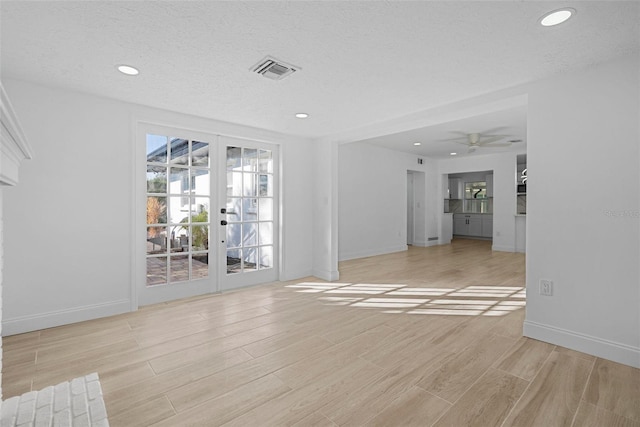 unfurnished living room featuring ceiling fan, french doors, a textured ceiling, and light wood-type flooring