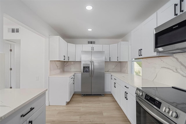 kitchen featuring backsplash, white cabinetry, light stone counters, and appliances with stainless steel finishes