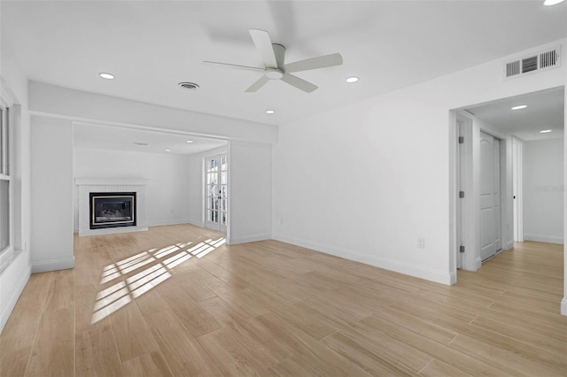 unfurnished living room featuring french doors, light wood-type flooring, a brick fireplace, and ceiling fan