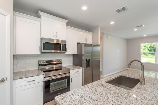 kitchen with white cabinetry, sink, light stone countertops, stainless steel appliances, and tasteful backsplash