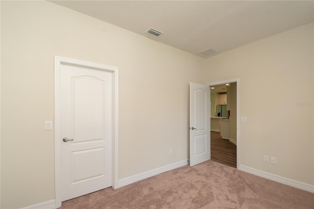 unfurnished bedroom with light carpet, stainless steel refrigerator with ice dispenser, visible vents, and baseboards