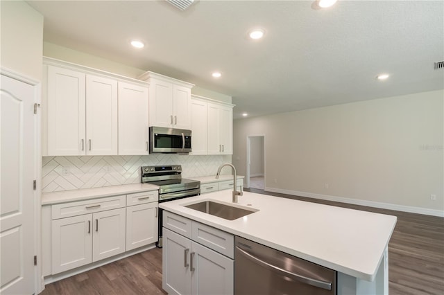 kitchen with light countertops, appliances with stainless steel finishes, white cabinets, a sink, and an island with sink