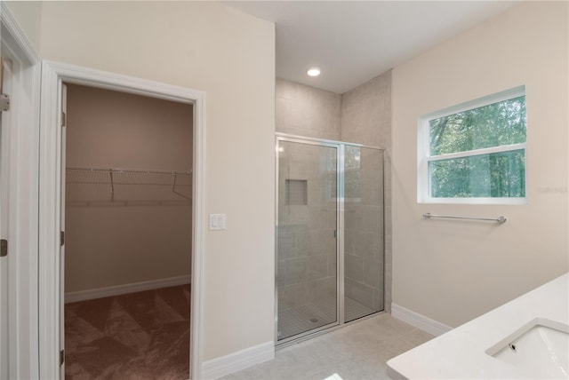 bathroom featuring baseboards, a walk in closet, a shower stall, a sink, and recessed lighting