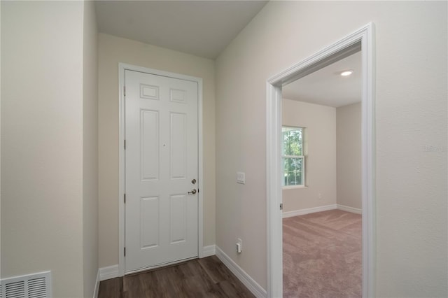 doorway featuring dark wood-style floors, baseboards, visible vents, and dark carpet