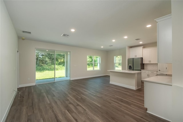 interior space with a center island with sink, tasteful backsplash, light countertops, open floor plan, and white cabinetry