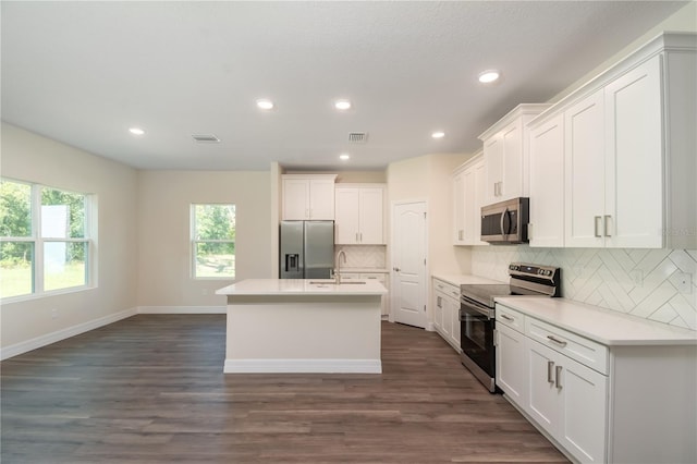 kitchen with light countertops, appliances with stainless steel finishes, a kitchen island with sink, and white cabinetry