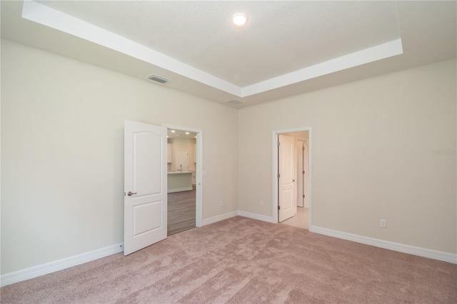 empty room with baseboards, a tray ceiling, visible vents, and light colored carpet