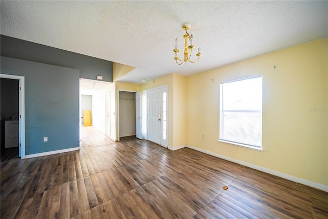 empty room with washer / dryer, a textured ceiling, dark hardwood / wood-style floors, and a notable chandelier