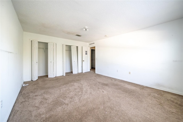 unfurnished bedroom featuring carpet, a textured ceiling, and two closets