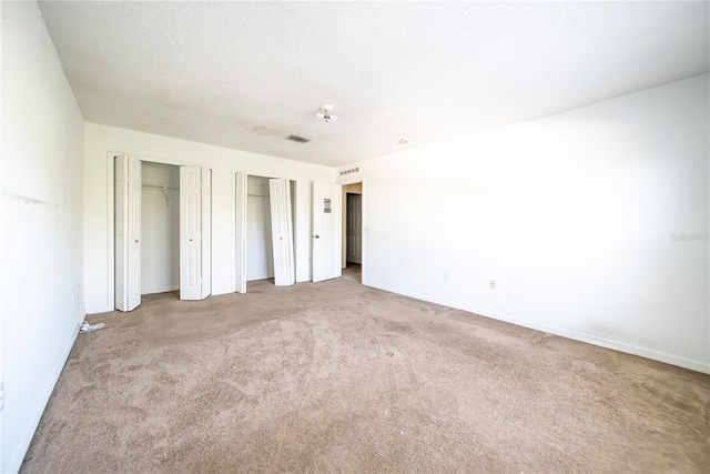 unfurnished bedroom with multiple closets, light carpet, and a textured ceiling