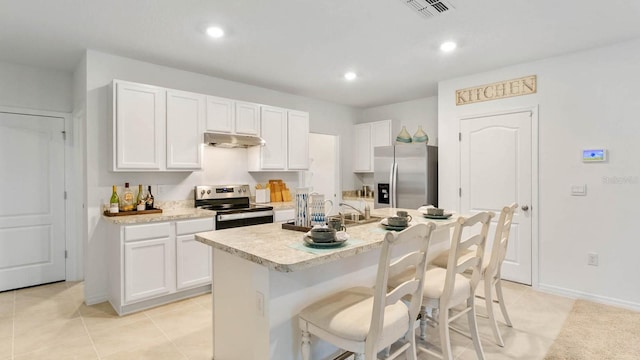 kitchen with stainless steel appliances, light tile patterned flooring, an island with sink, a kitchen bar, and white cabinets