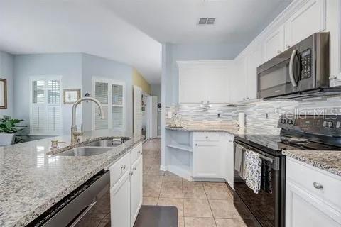 kitchen featuring light stone counters, stainless steel appliances, sink, light tile patterned floors, and white cabinetry